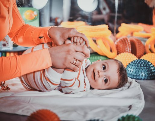 Educator sitting on the floor with a smiling baby and a bead maze toy
